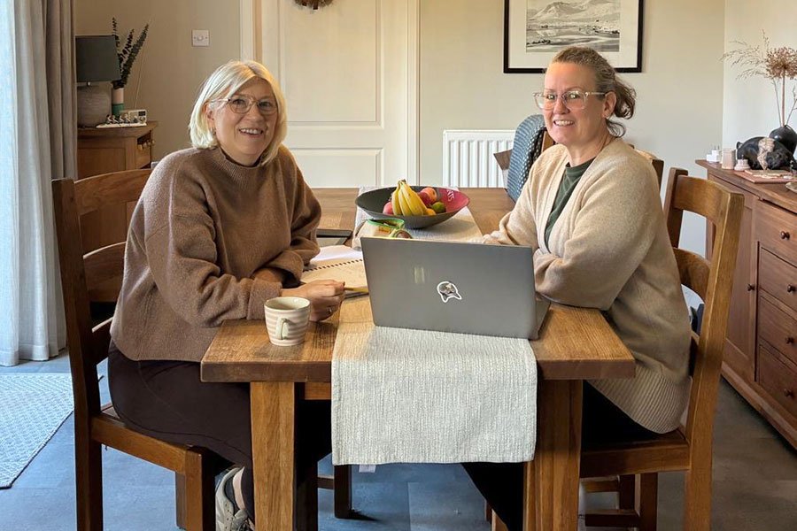 Lilian and Kirsty sitting working together at a table with a laptop